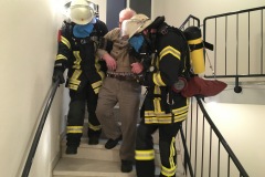 Eine Person wird über das Treppenhaus gerettet. Um realistische Sichtbedingungen durch Rauch zu simulieren, wurden die Masken der Atemschutzgeräteträger mit Folie abgedeckt.