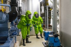 Feuerwehrleute in Chemikalienschutzanzügen führen im Technikraum Messungen durch.