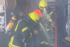 Einsatzkräfte unter Atemschutz retten eine Person aus einem verrauchten Nebengebäude.