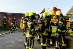 Einsatzkräfte unter Atemschutz bereiten sich auf ihren Einsatz zur Menschenrettung aus dem vollkommen verqualmten Büroanbau vor.