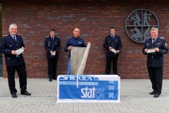 Vertreter der Ortsfeuerwehren empfangen aus der Materialspende gefertigte Mund-Nasen-Schutze. Stadtbrandmeister Peter Schmidt (rechts) dankt stellvertretend Markus Grefe (Mitte) von der Firma Statex.